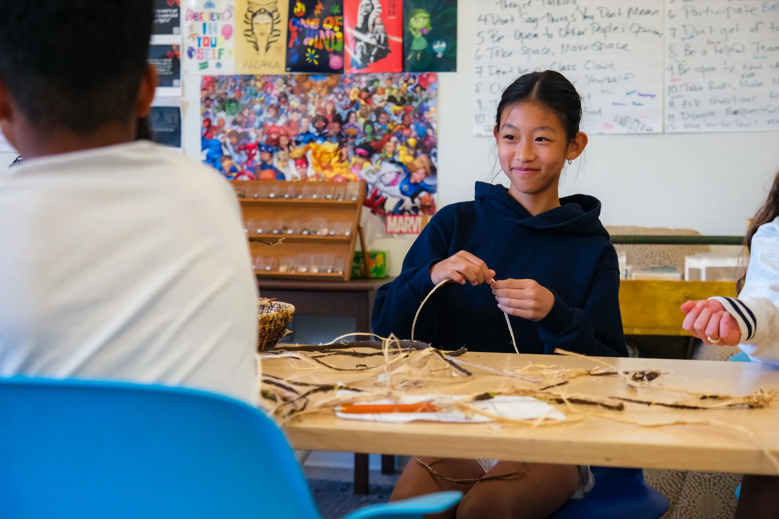 A Middle School student smiles while weaving a basket in class