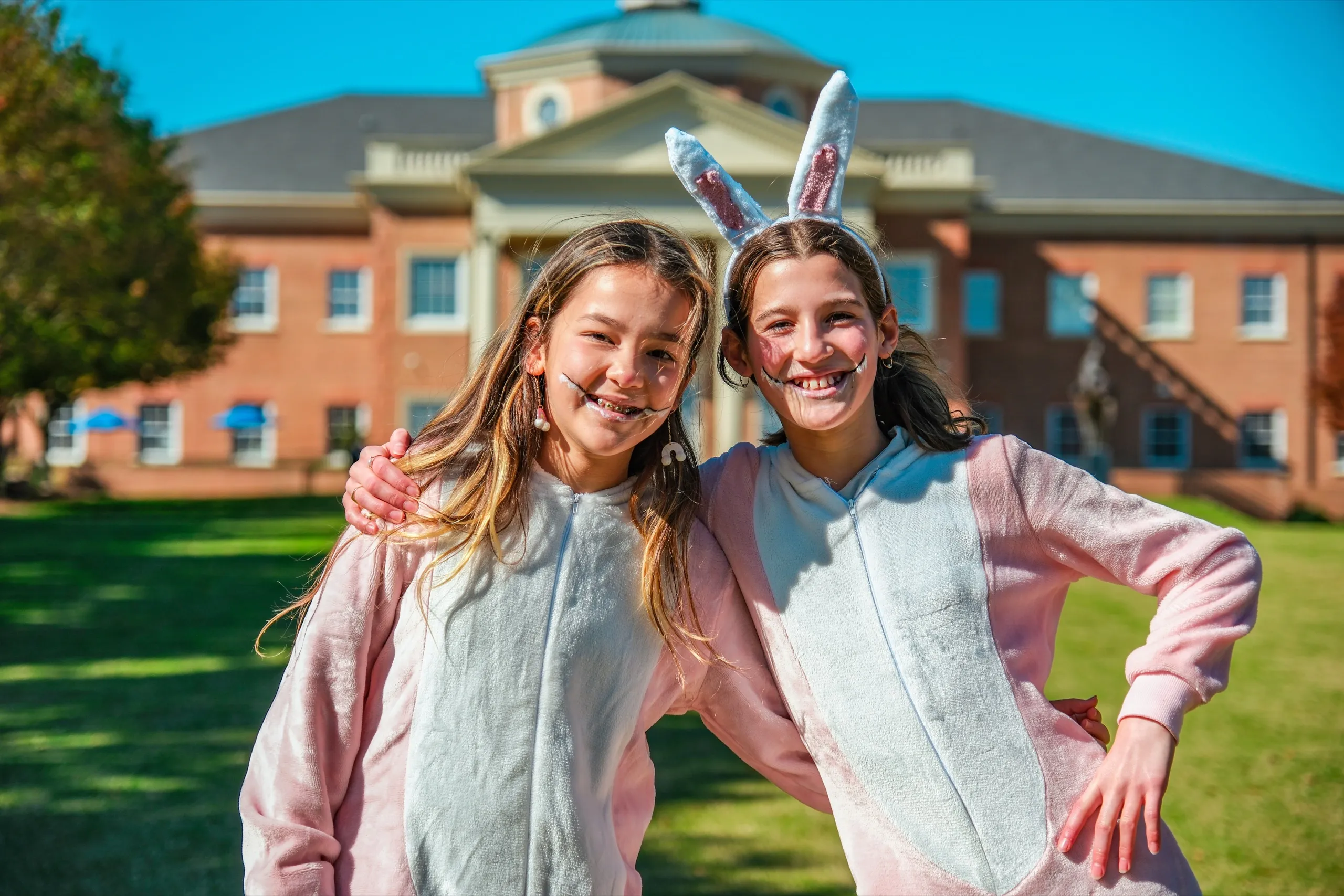 Two Middle School students in bunny costumes smile in front of the main building on Halloween