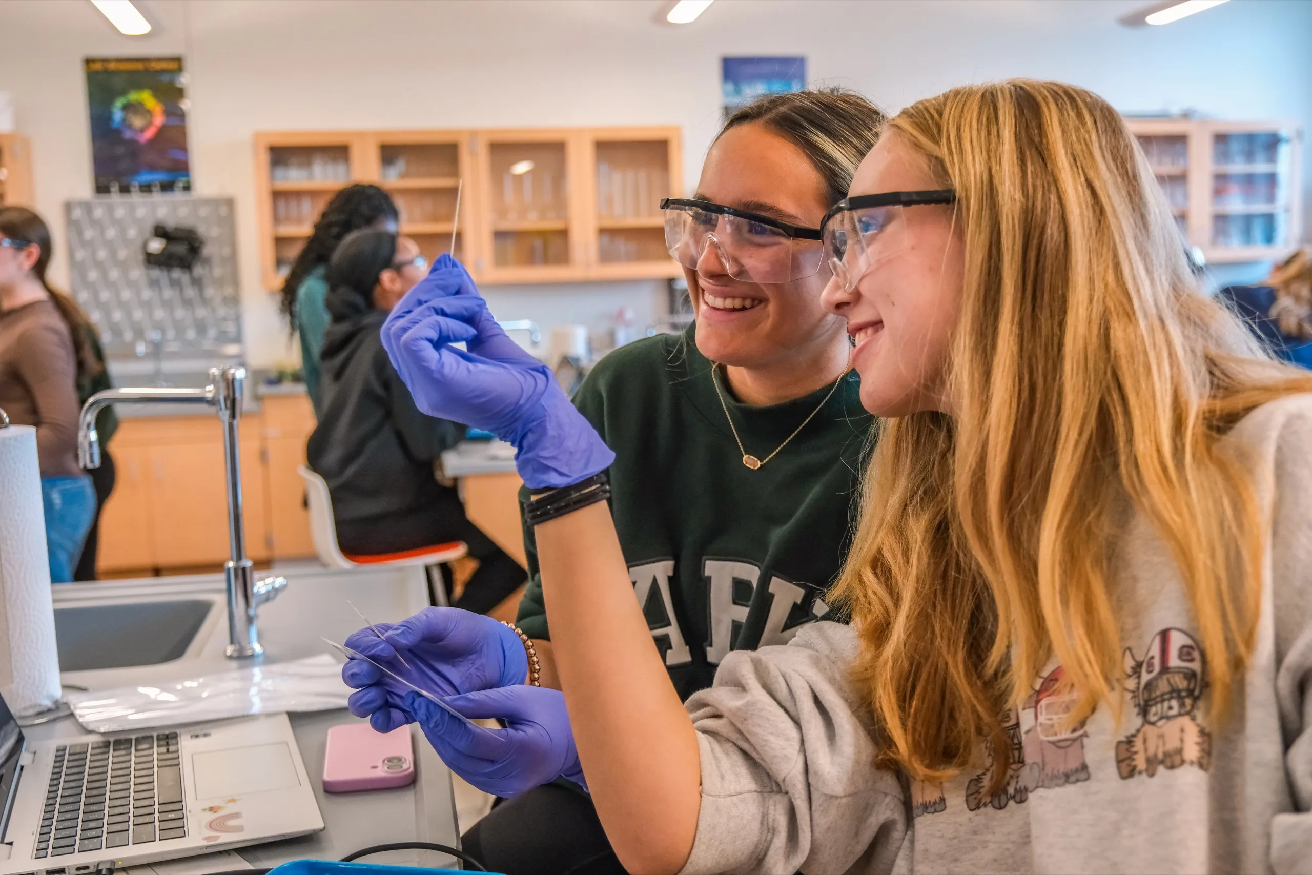 Two Upper School students in safety goggles laugh during a chemistry lab