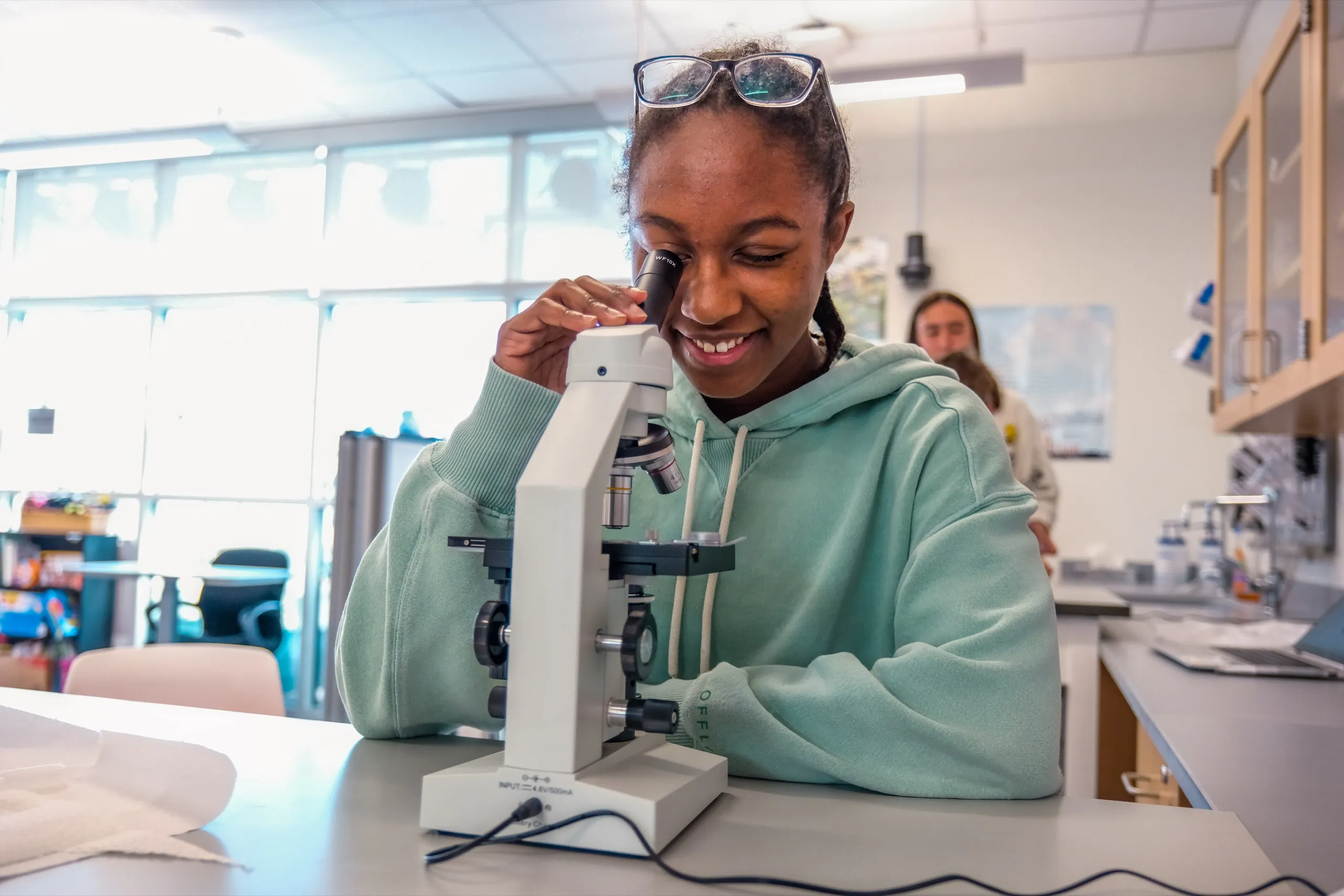 A student smiles as she looks into a microscope in a science lab
